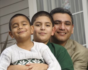 Latino father and two young sons sitting together in front of a house