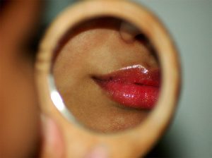 Woman looking in a mirror with red lipstick on.