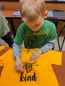 Ablonde haired boy making a bee kind t-shirt.