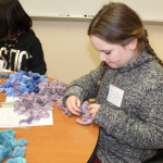 Girl with brown hair and gray sweater working on a 4-H project at Family Learning Day